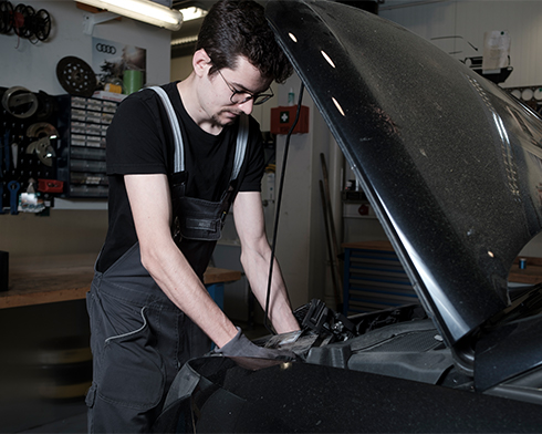 Ein Mechaniker, der bei geöffneter Motorhaube den Innenraum des Fahrzeuges checkt